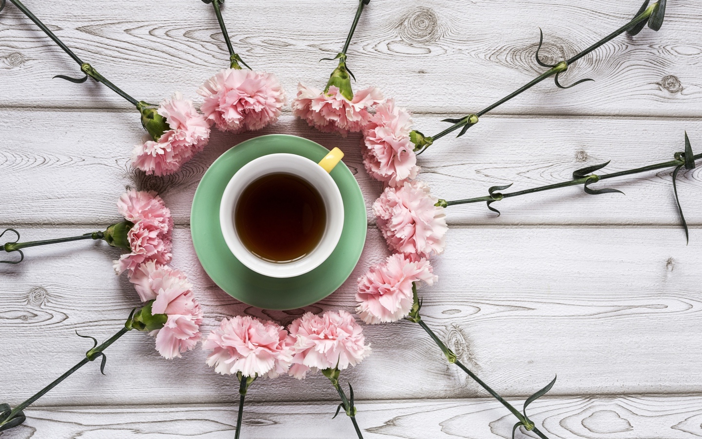 Розовые гвоздики с чашкой чая на деревянном столе 
