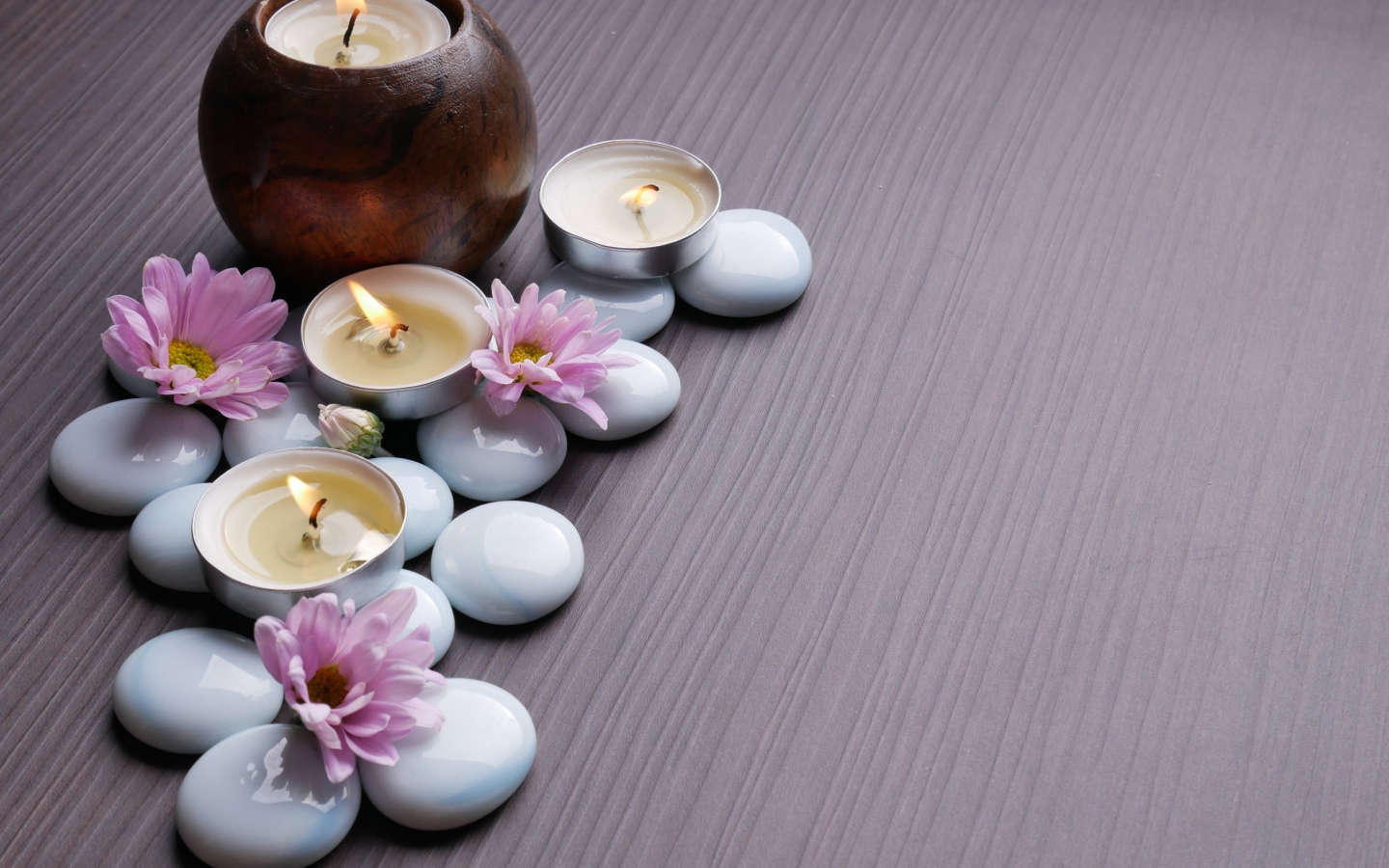 Камни с хризантемами и зажженными свечами на столе 