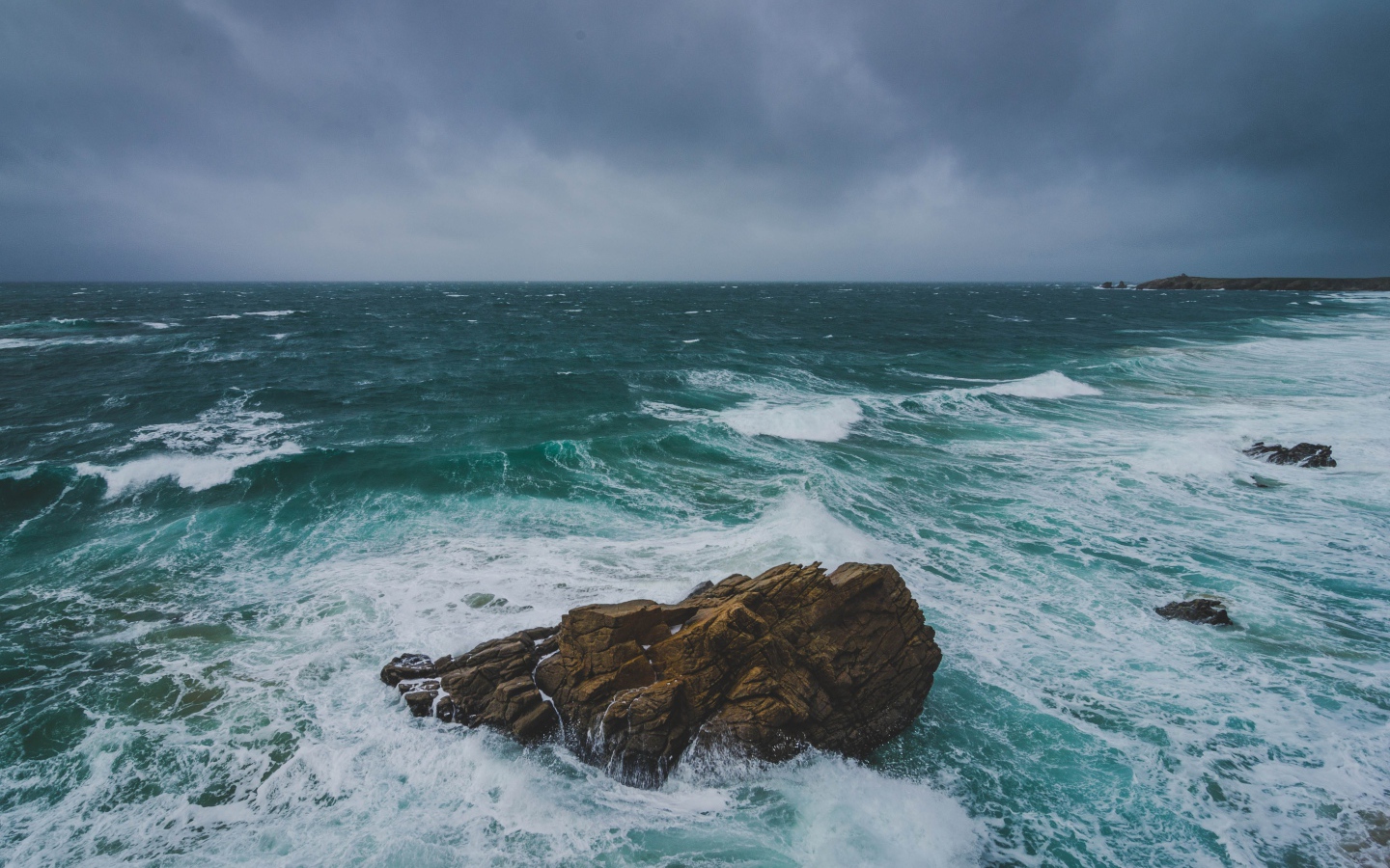 Большой камень омывают белые волны океана 