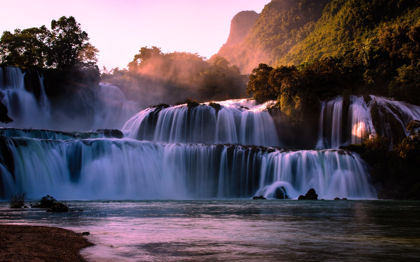 Каскадный водопад стекает по камням в лучах солнца 
