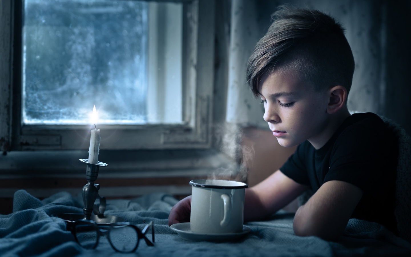 Маленький мальчик сидит за столом при свете свечи 