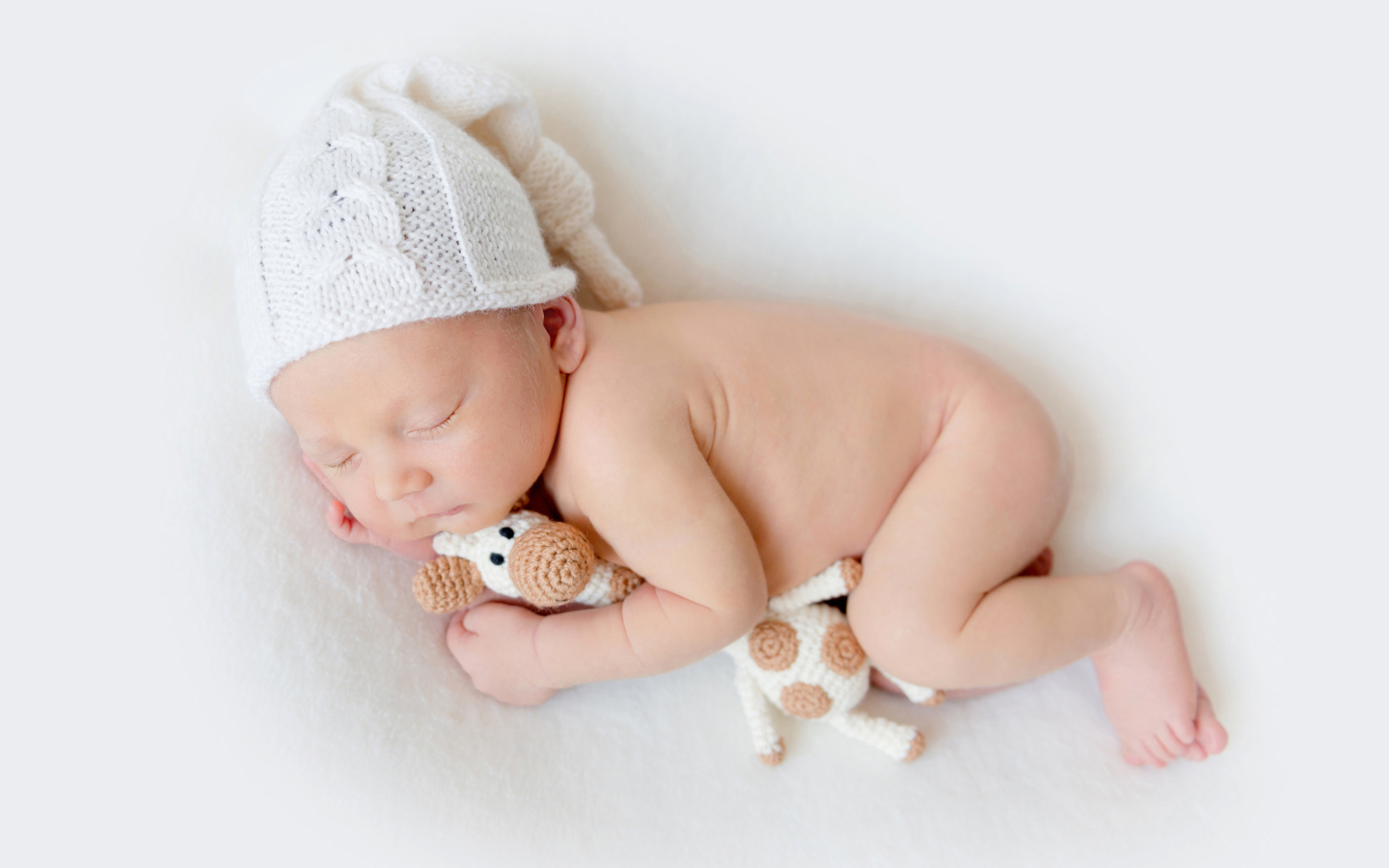 Младенец в шапке с игрушкой на белом фоне