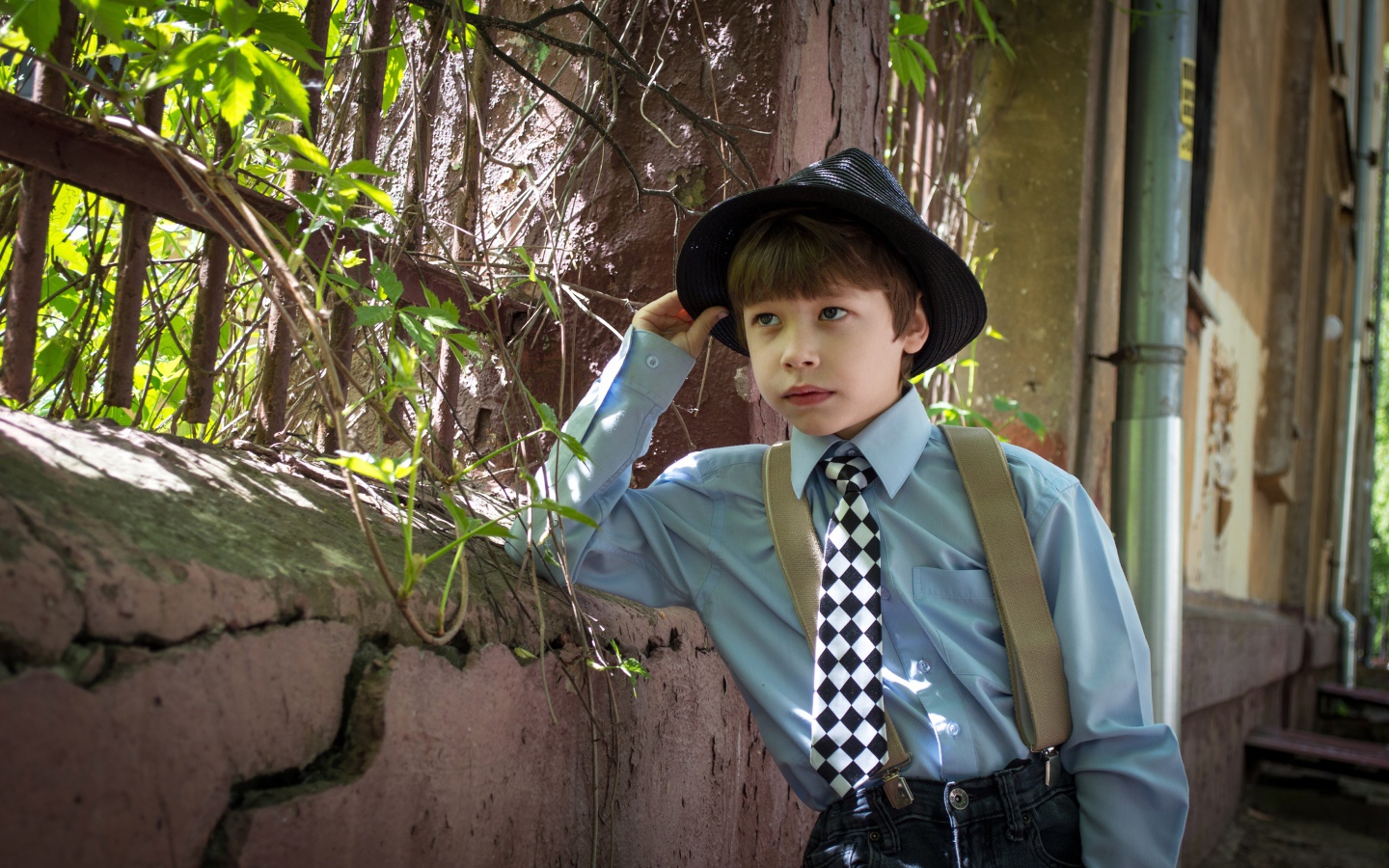 Красивый мальчик в шляпе стоит у забора 