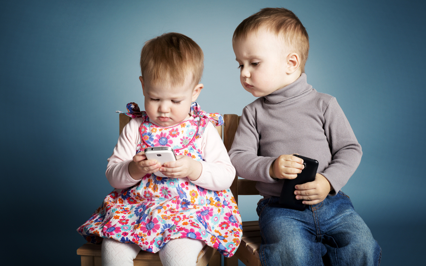 Маленькие мальчик  и девочка с телефонами на сером фоне 