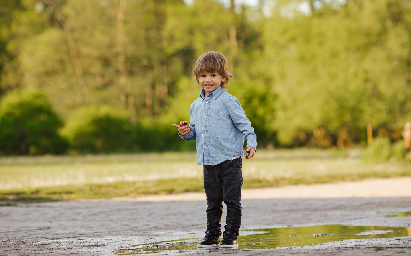Маленький мальчик стоит в луже на дороге 