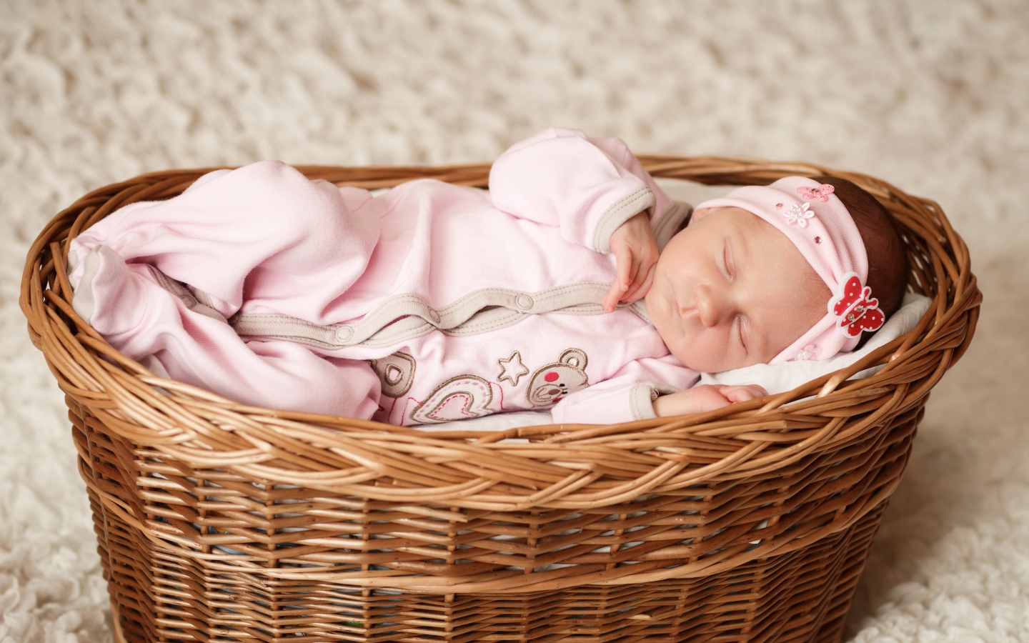 Маленькая новорожденная девочка в розовом костюме спит в корзине 
