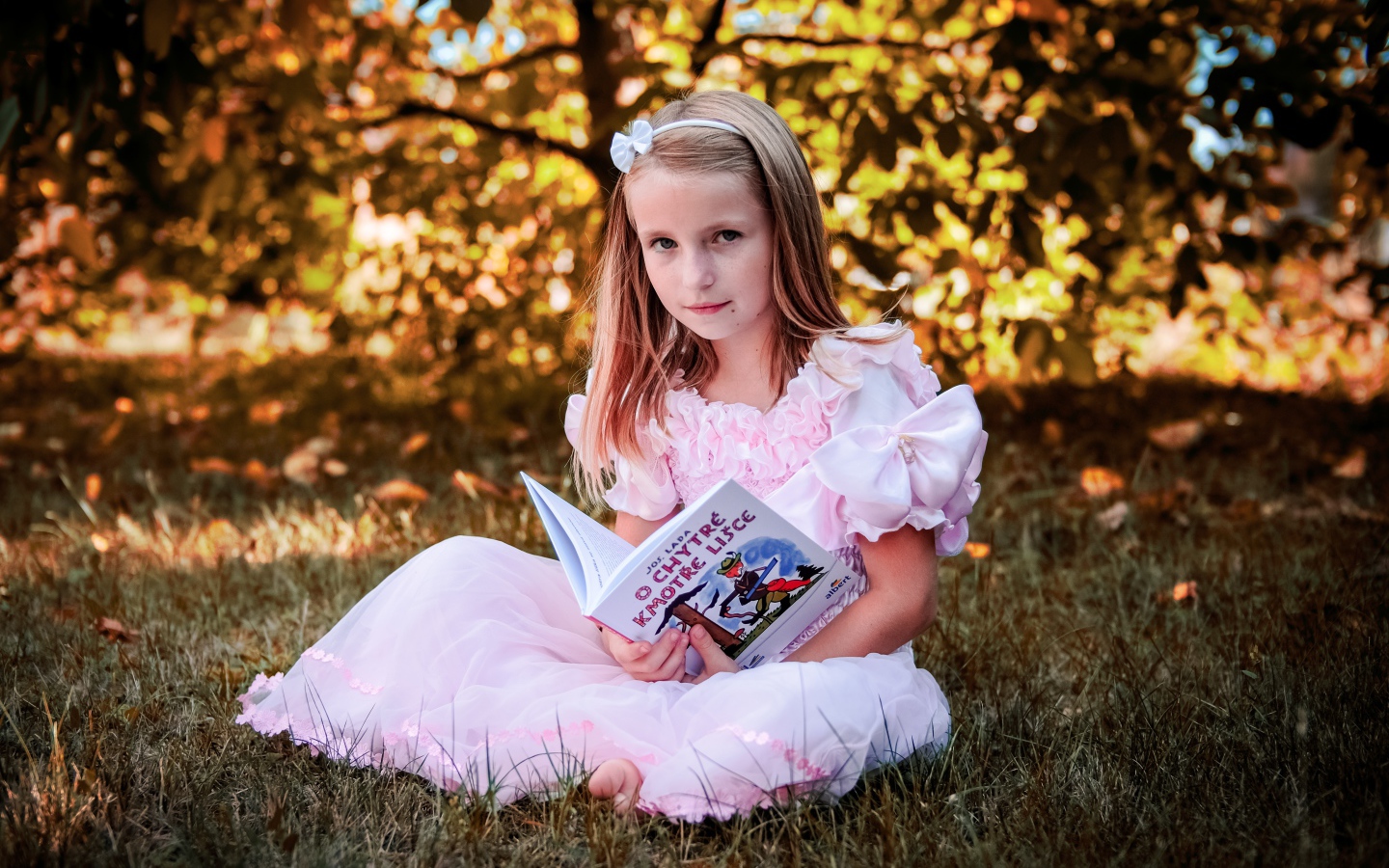 Маленькая принцесса сидит на траве с книгой
