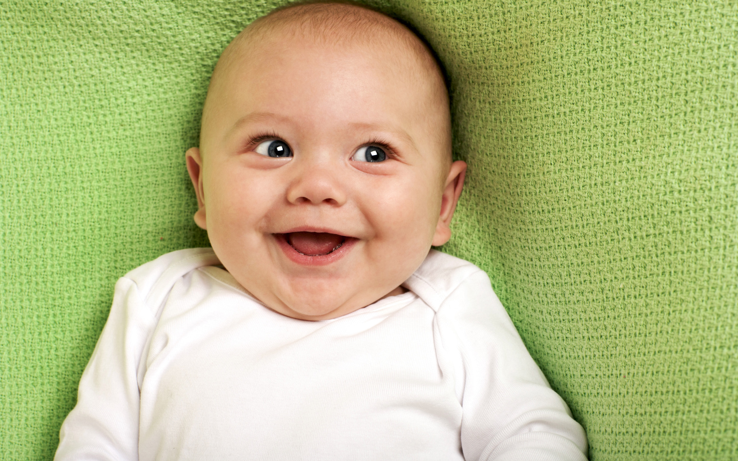 Улыбающийся маленький ребенок на зеленом покрывале 