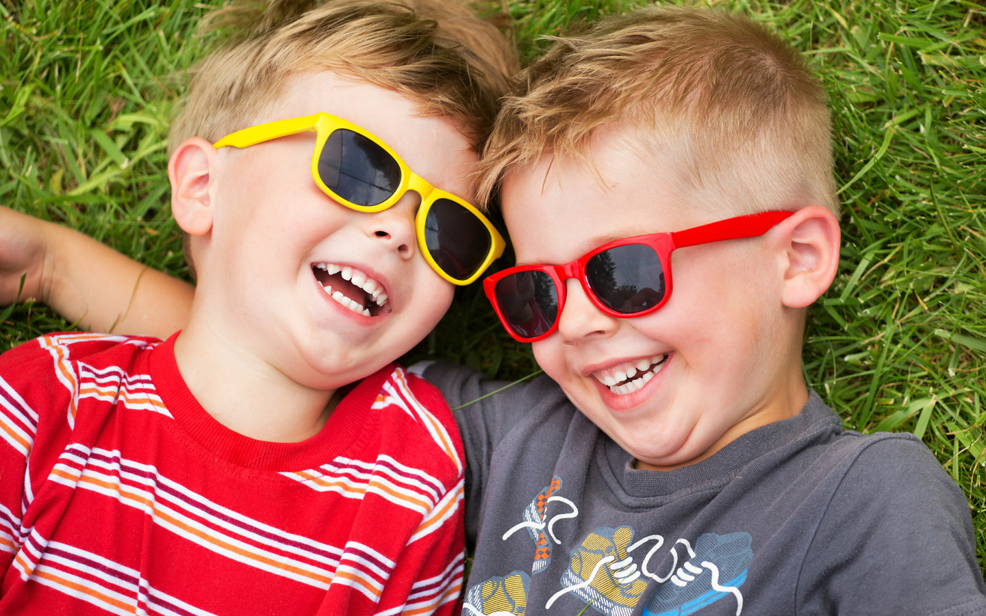 Два улыбающихся мальчика в очках на зеленой траве 