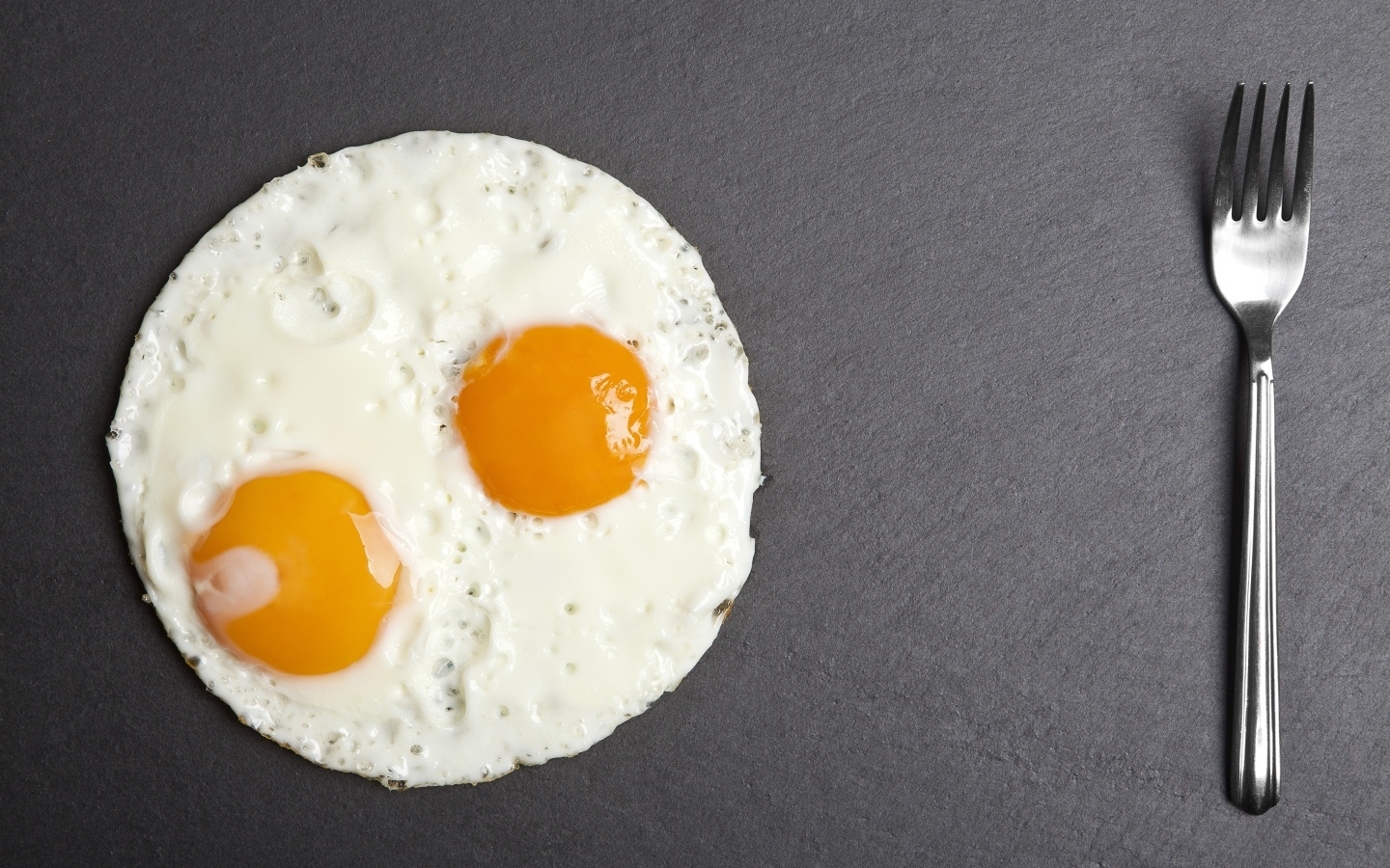 Яичница глазунья с вилкой на сером столе