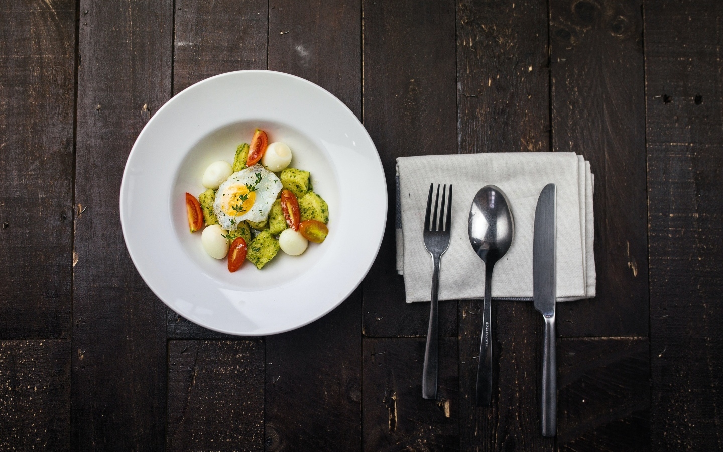 Яичница с овощами в белой тарелке на столе со столовыми приборами