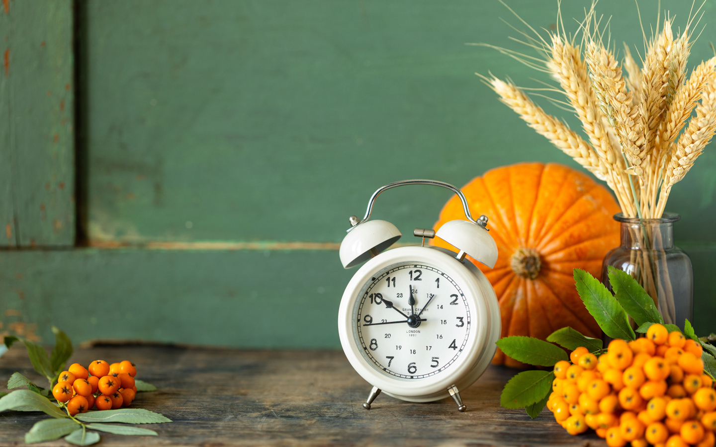 Будильник на столе с тыквой и ягодами рябины