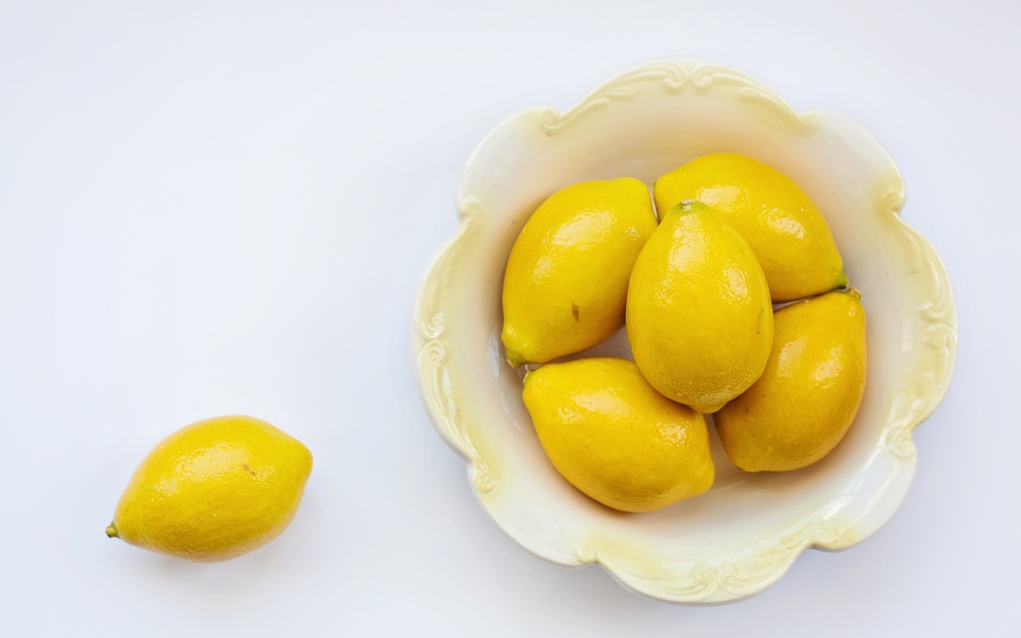 Крупные желтые лимоны в тарелке на белом фоне