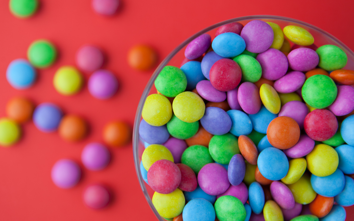 Разноцветные конфеты в стакане на красном столе