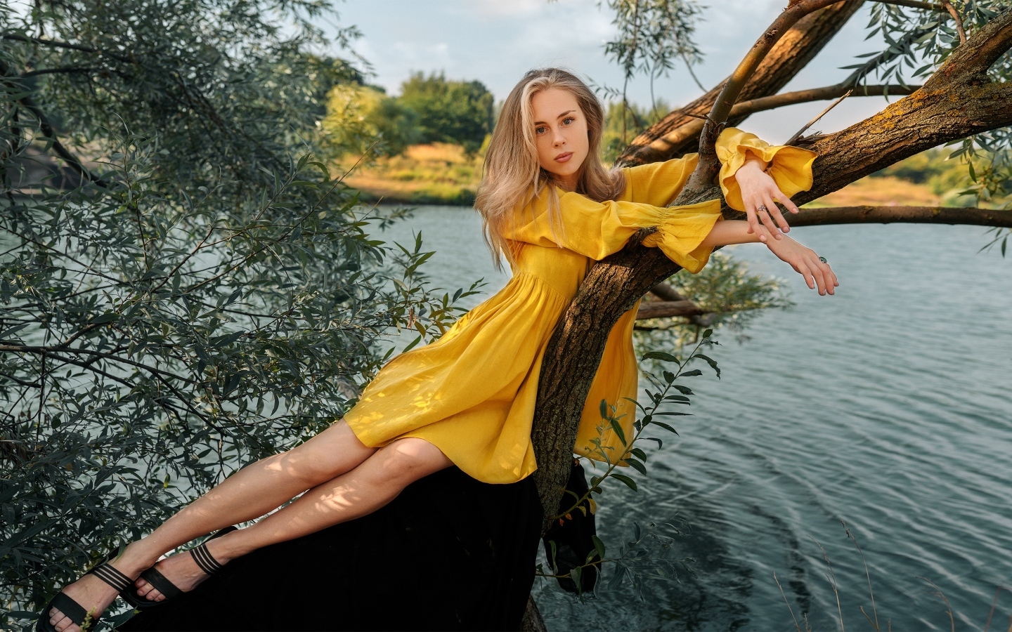 Красивая девушка в желтом платье лежит на дереве у воды
