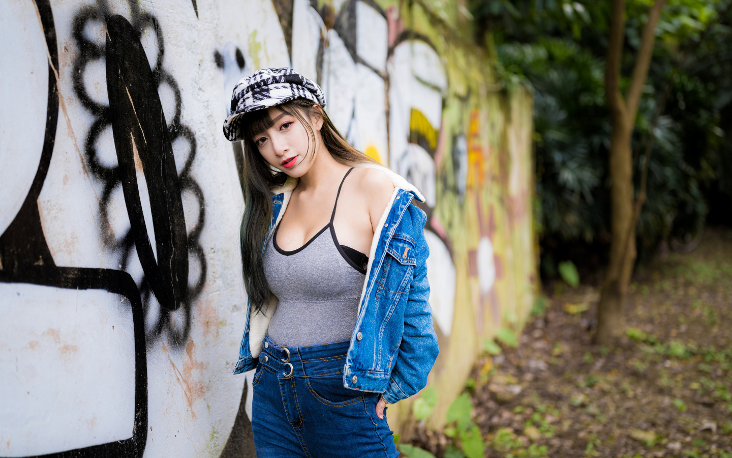 Девушка азиатка в джинсовой куртке стоит у стены