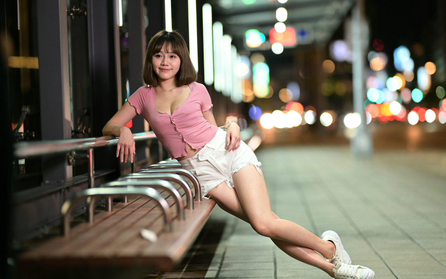 Азиатка в коротких белых шортах сидит на остановке