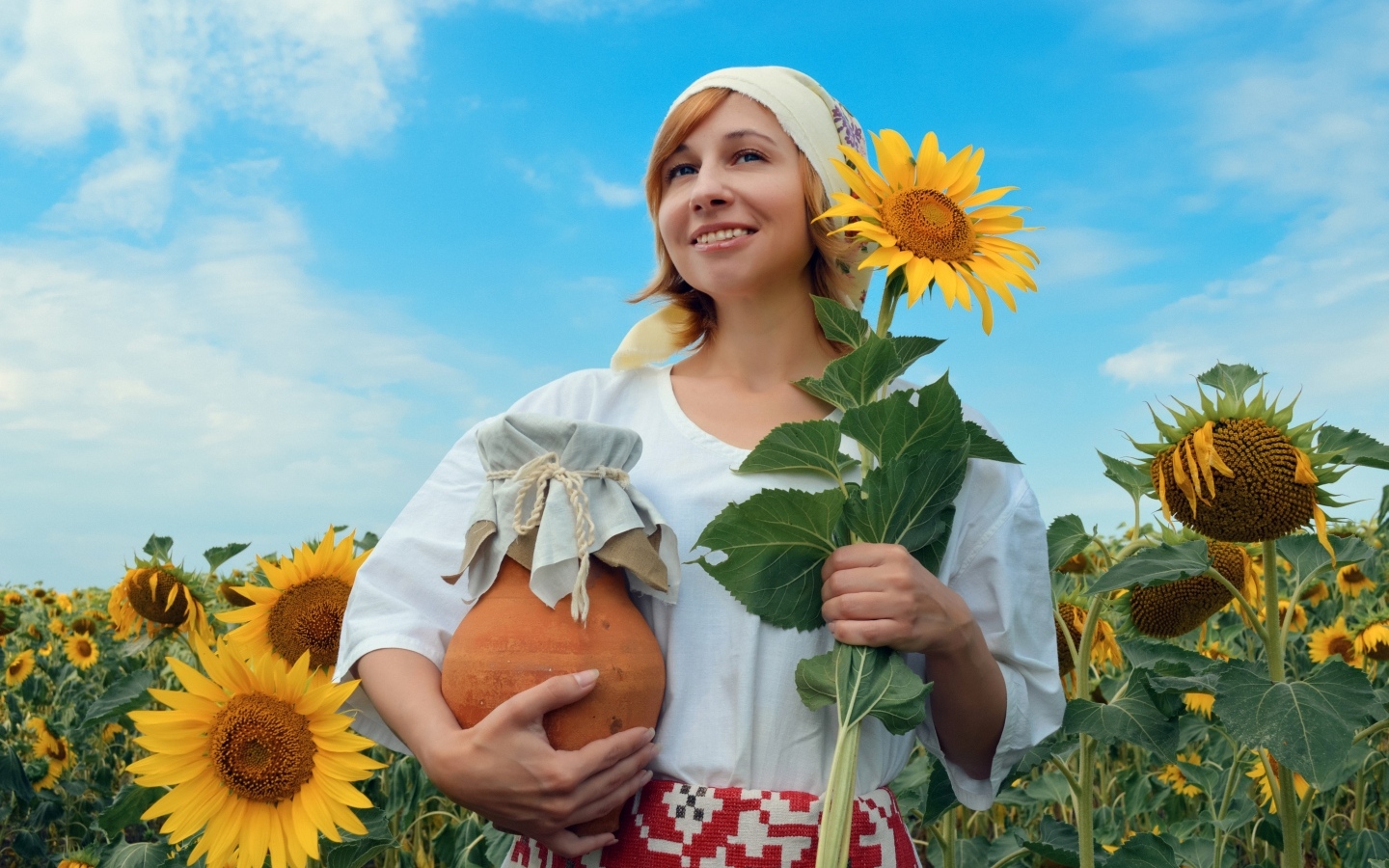 Красивая девушка с кувшином на поле с подсолнухами