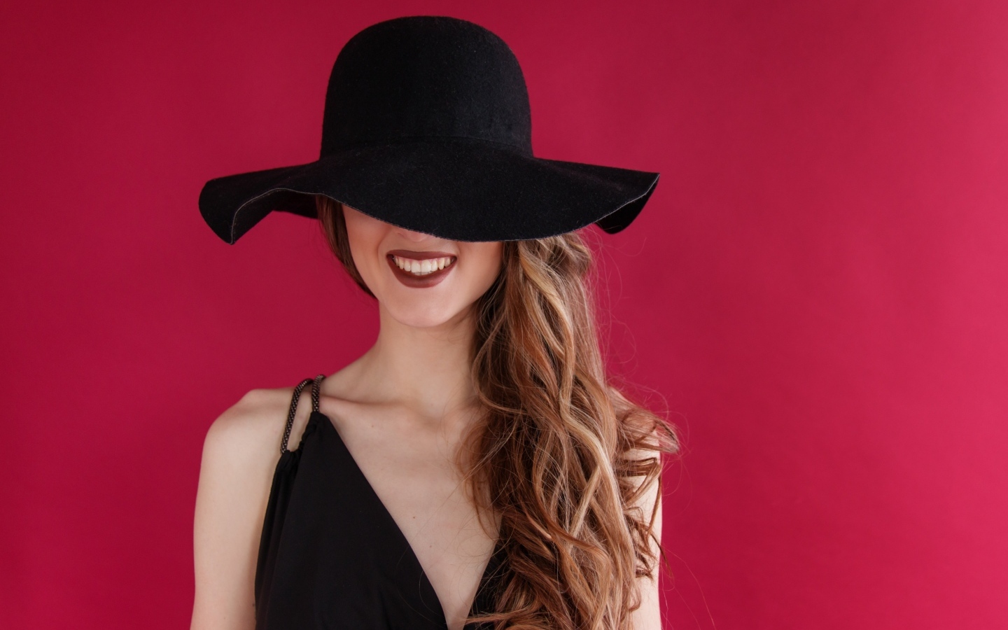 Черная шляпа на лице у девушки на розовом фоне