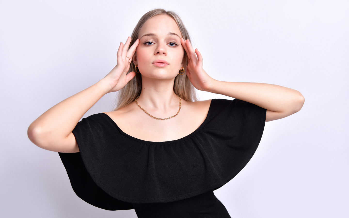 Девушка в черном платье с руками у головы на белом фоне