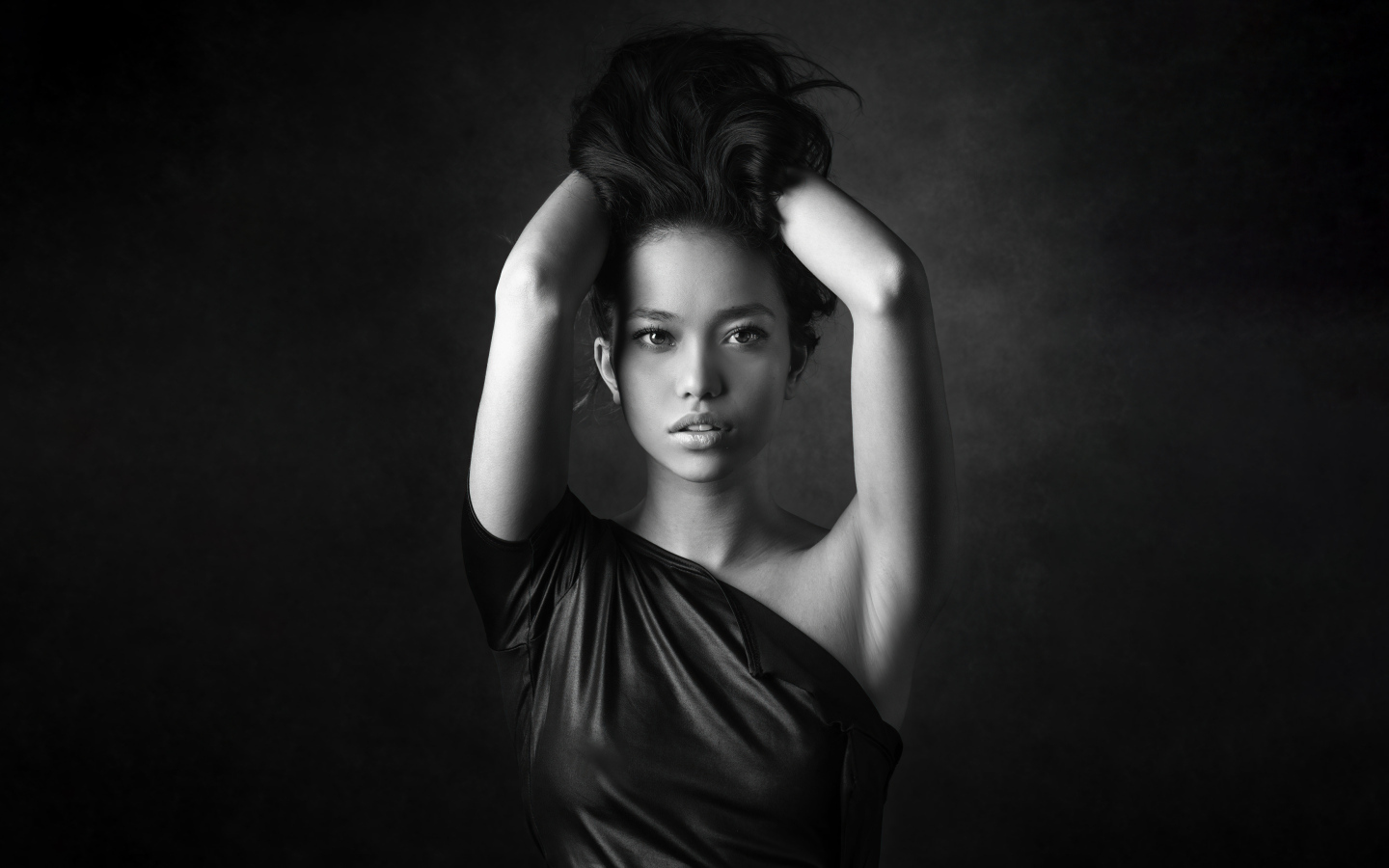 Девушка модель с руками в волосах  у стены