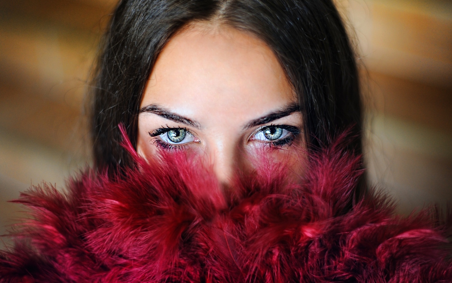Девушка с красивыми глазами закрыла лицо красными перьями
