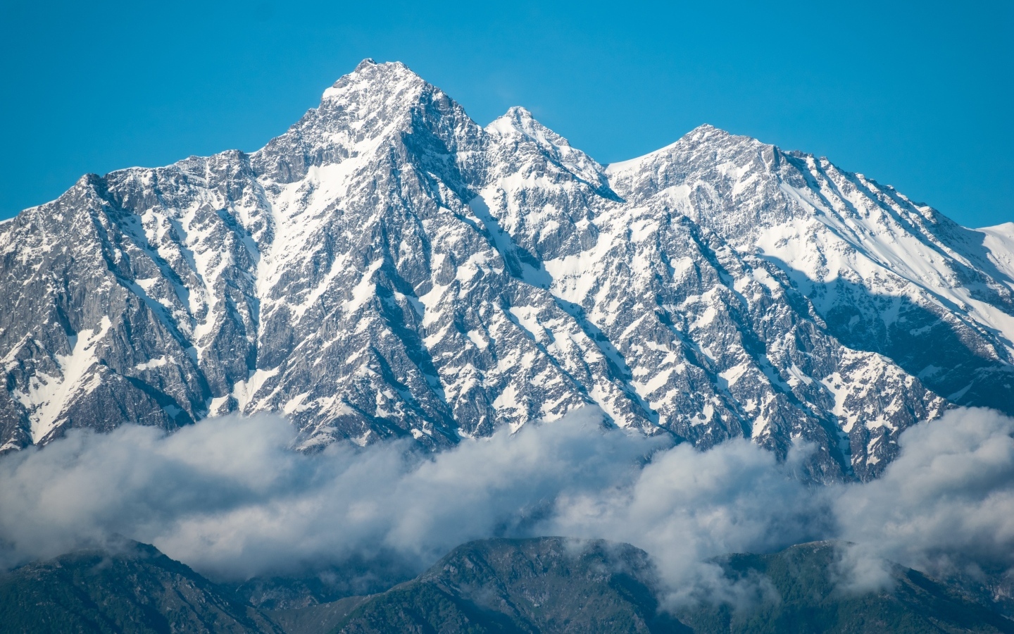 Высокие заснеженные горы в тумане под голубым небом