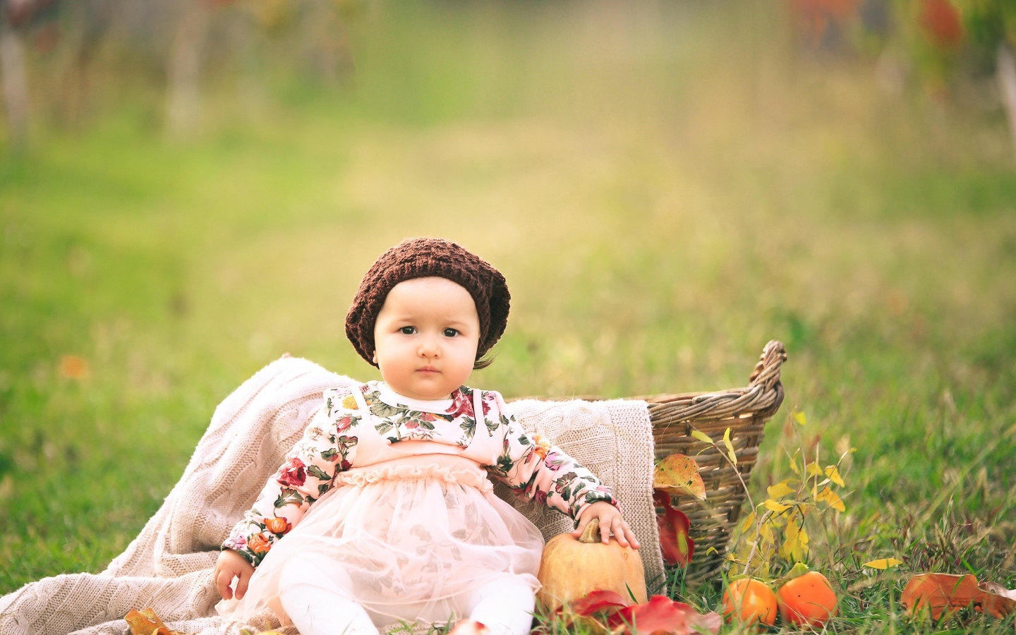 Милая маленькая девочка в шапке сидит на траве 