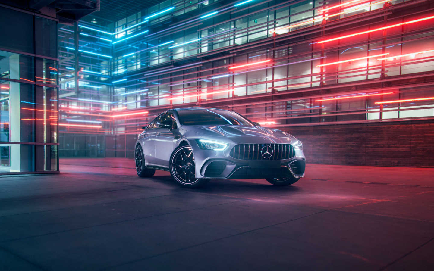 Серебристый автомобиль Mercedes AMG GT4 на фоне здания