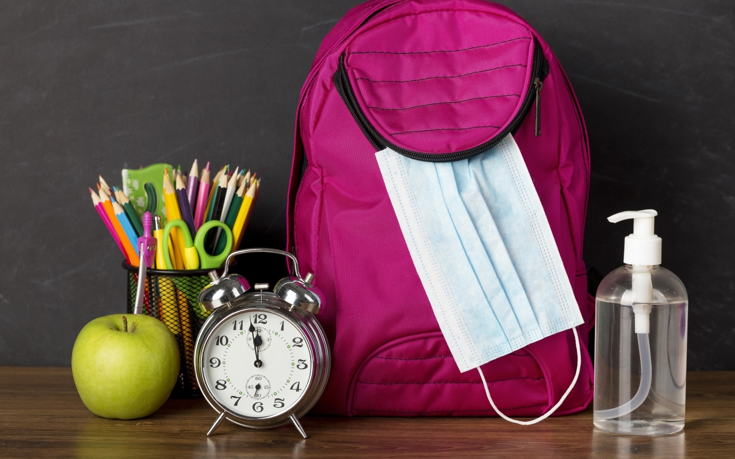 Рюкзак на столе с будильником, ручками и яблоком