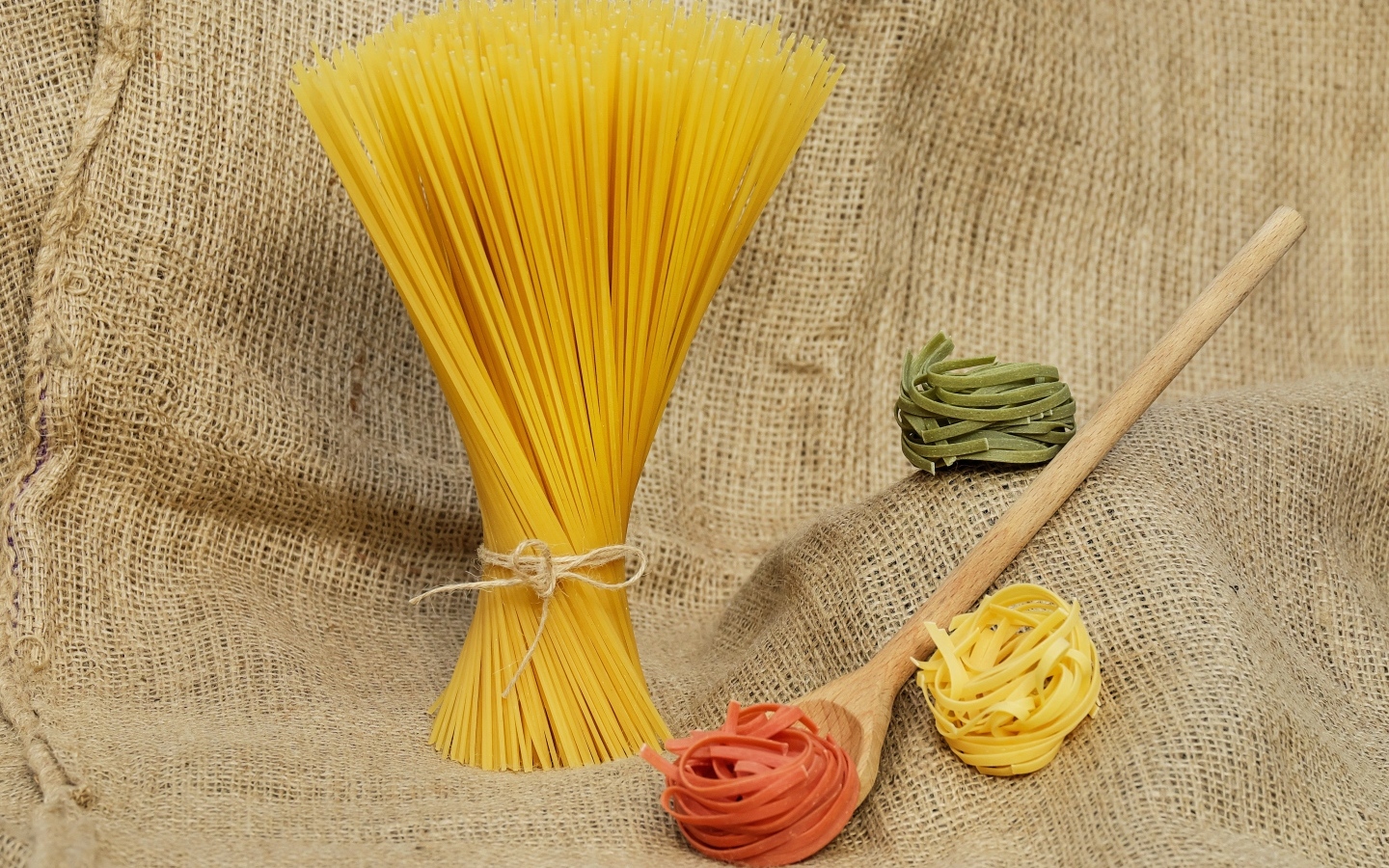 Разноцветные макаронные изделия с деревянной ложкой на мешке