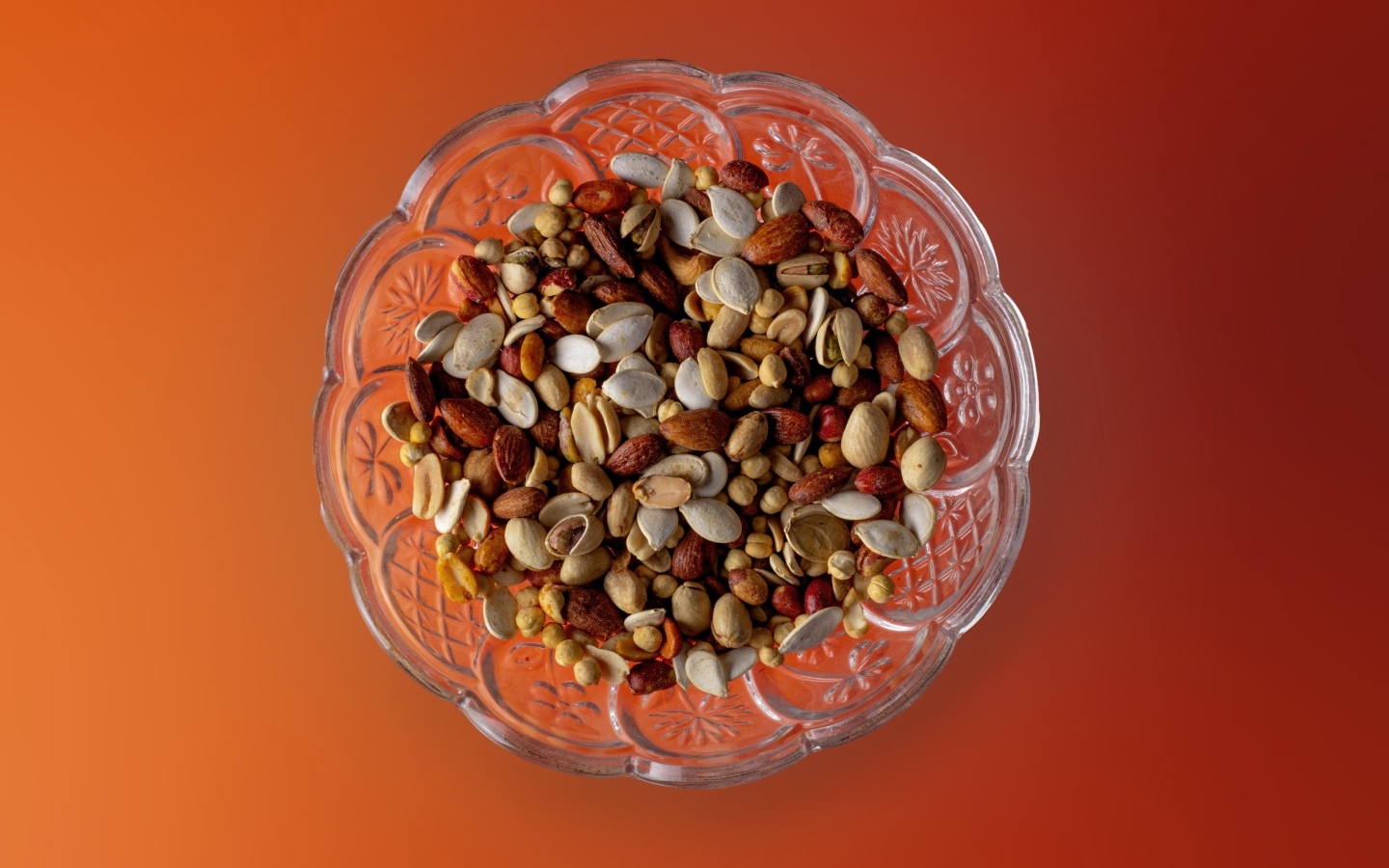 Семечки и орехи в стеклянной вазе на оранжевом фоне