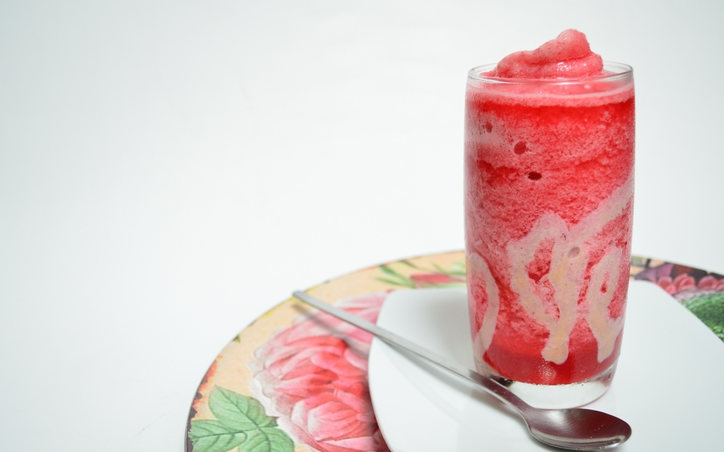 Стакан красного ягодного смузи на столе с чайной ложкой