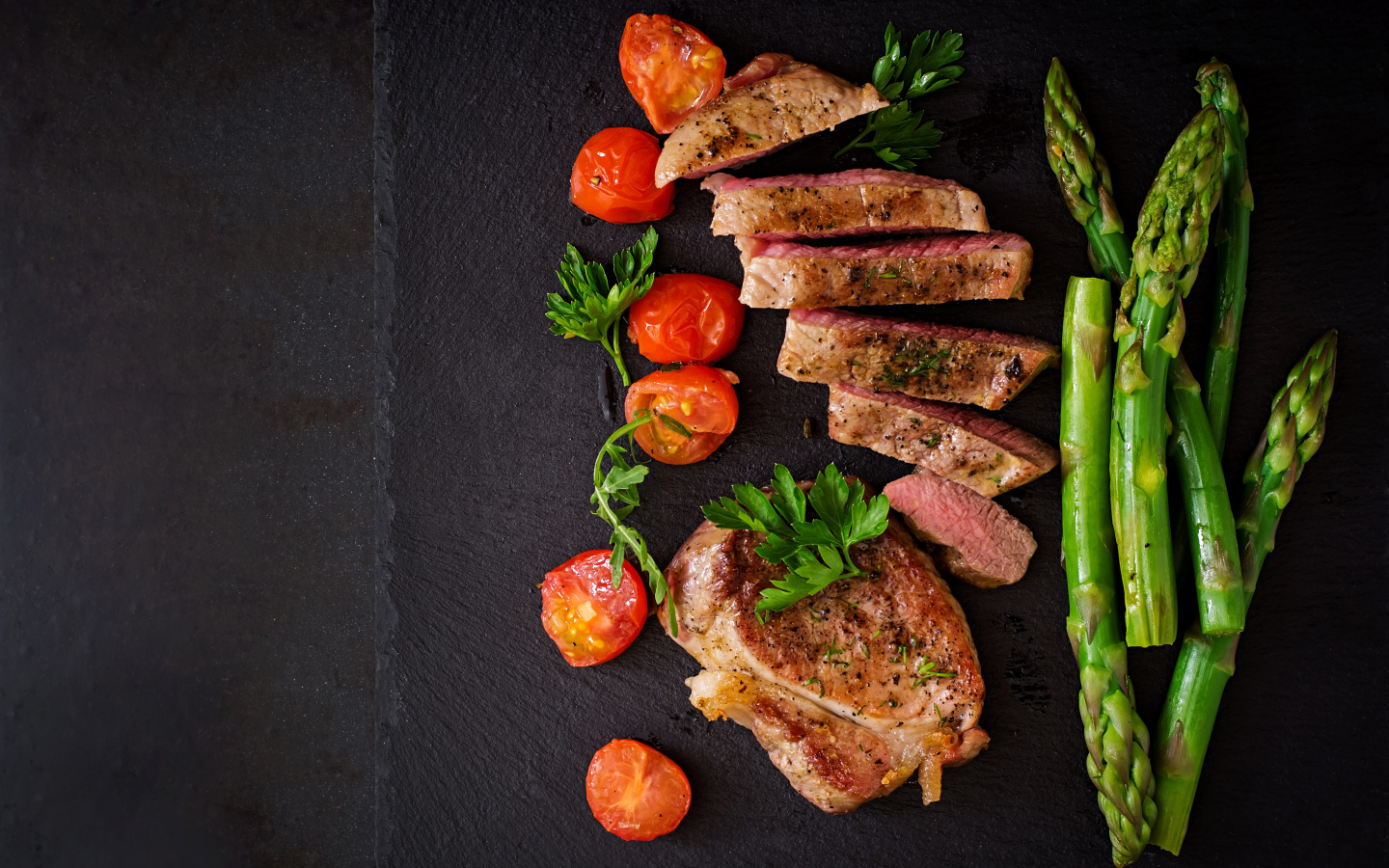 Нарезанный кусок мяса с помидорами и зеленой спаржей