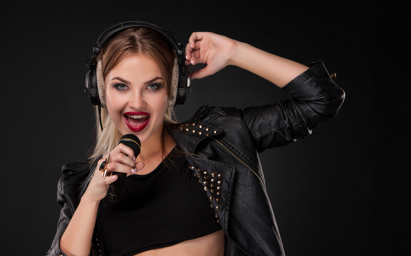 Девушка в черной кожаной куртке поет в микрофон