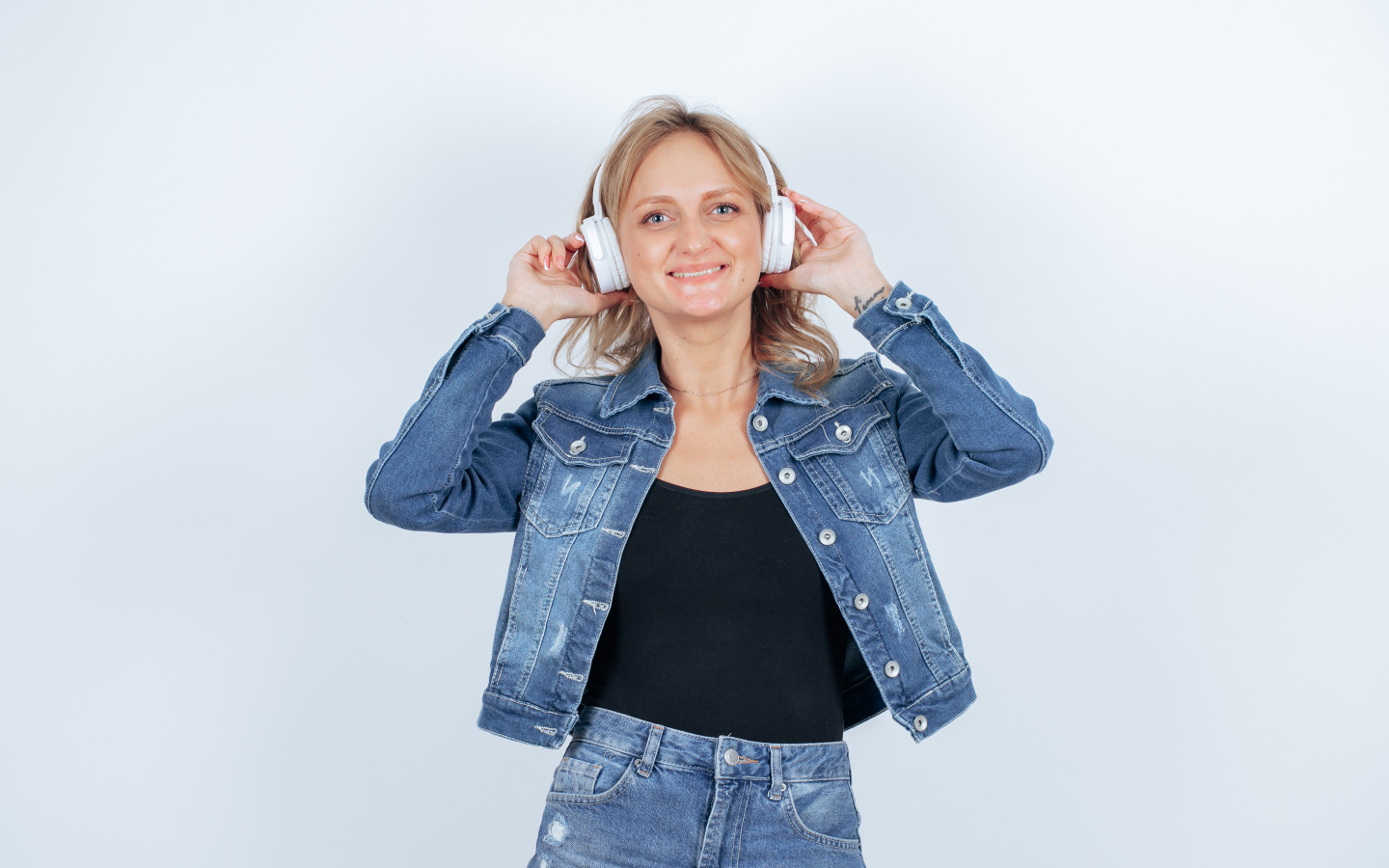 Девушка в джинсовом костюме с наушниками на голове на фоне стены