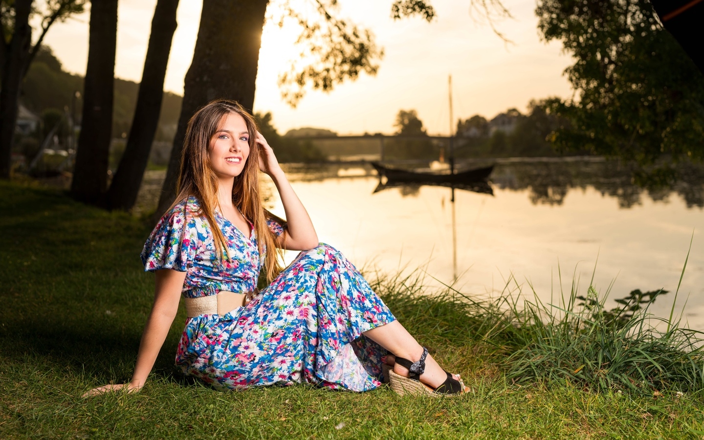 Милая девушка в платье сидит на берегу реки в парке
