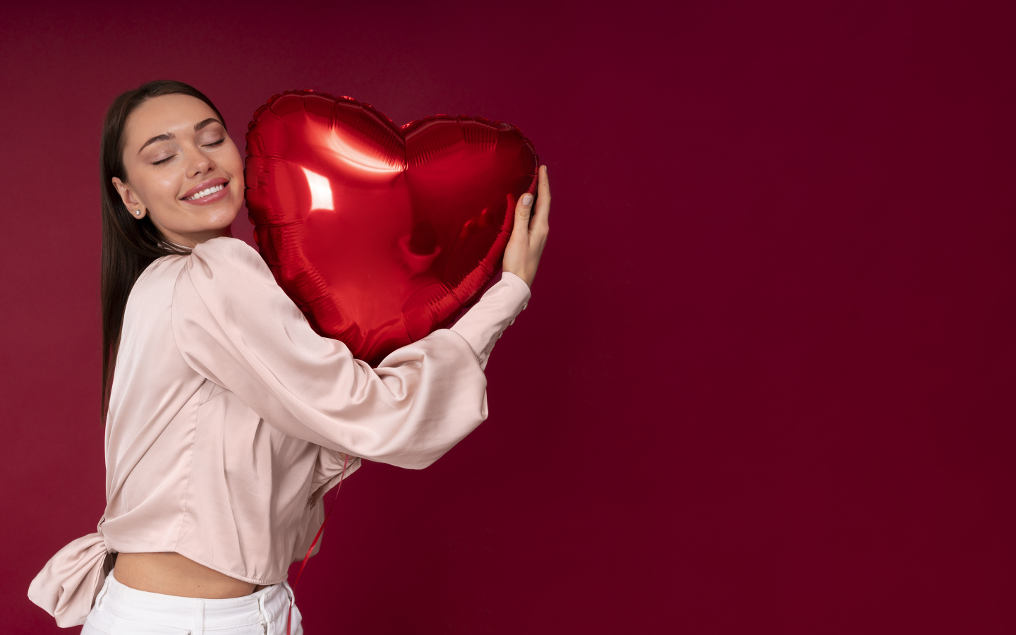 Девушка держит шарик в форме сердца на красном фоне
