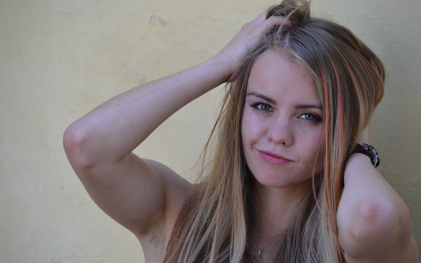 Девушка с руками в волосах у стены