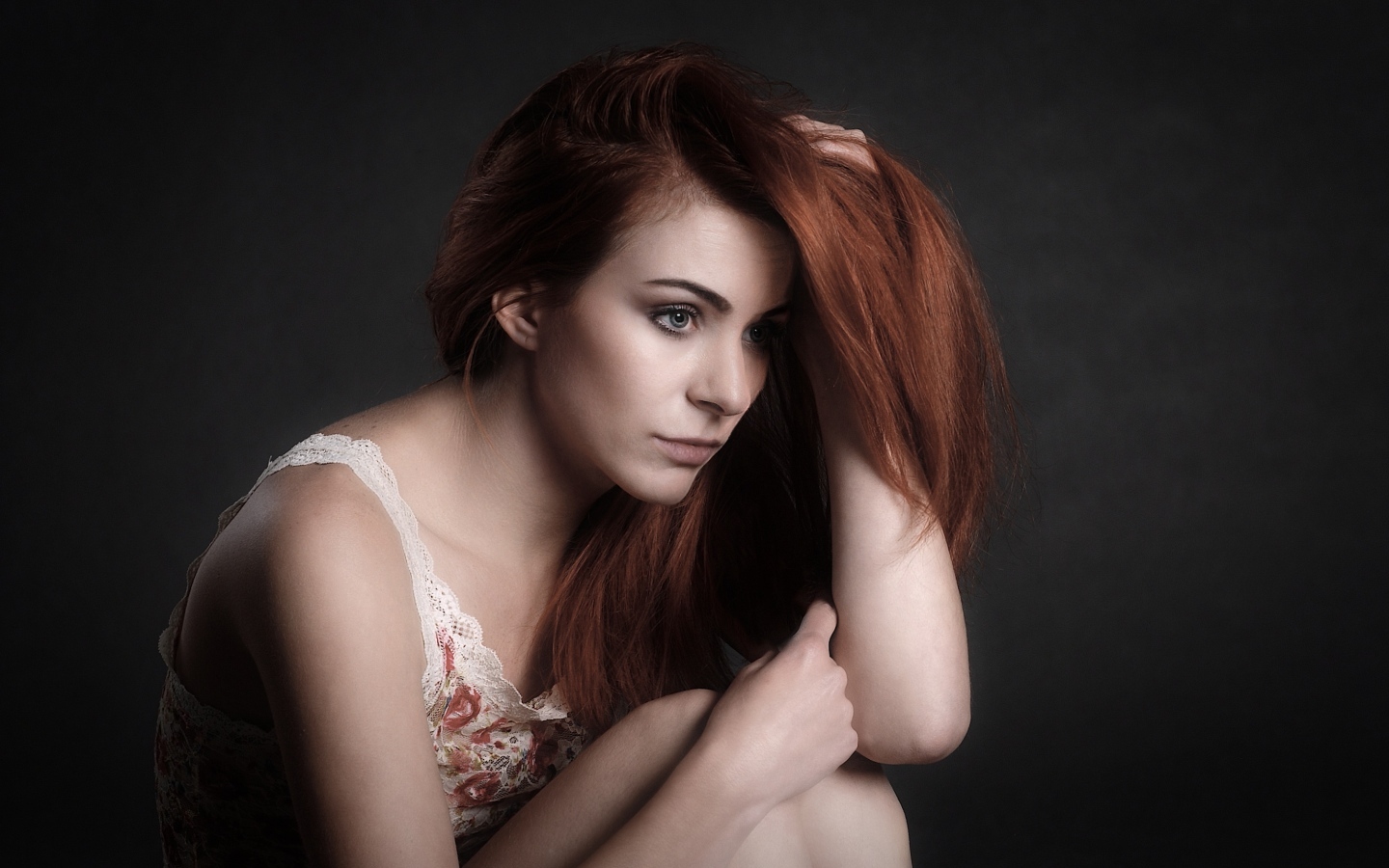 Задумчивая рыжеволосая девушка на сером фоне