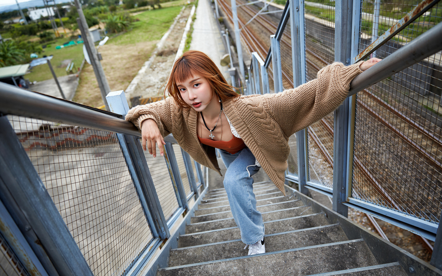 Рыжеволосая азиатка в кофте стоит на ступеньках