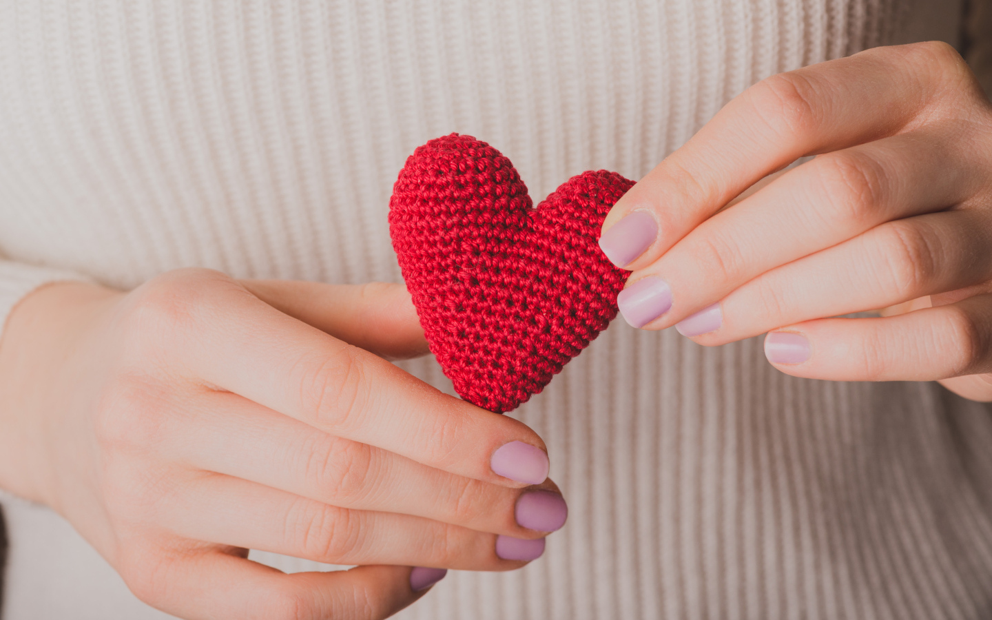 Девушка держит в руке вязаное красное сердце