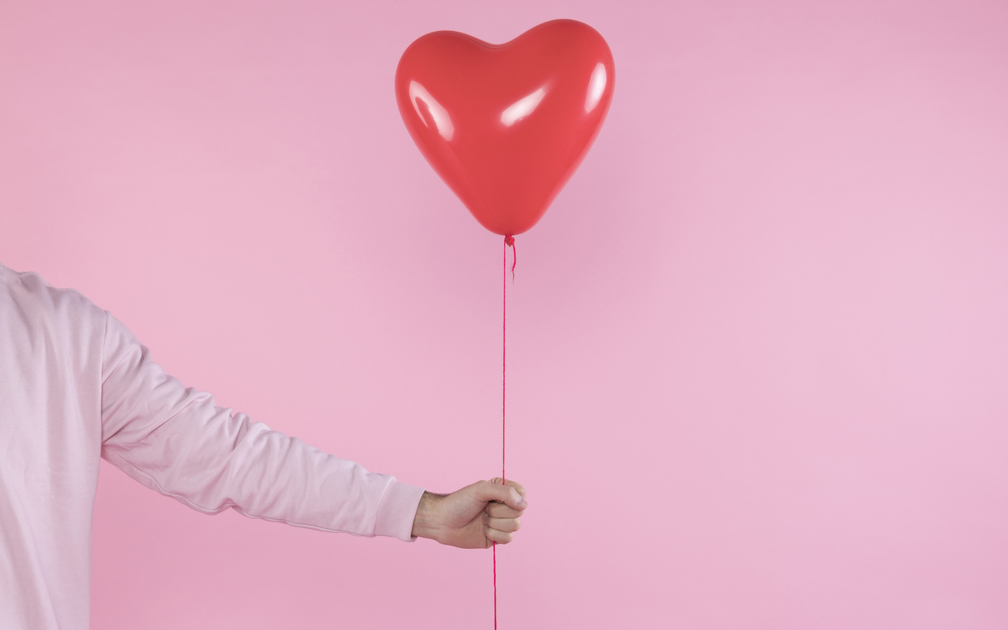 Шарик в форме сердца в руке на розовом фоне