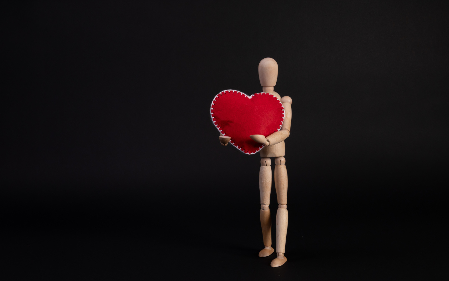 Марионетка держит красное сердце на черном фоне
