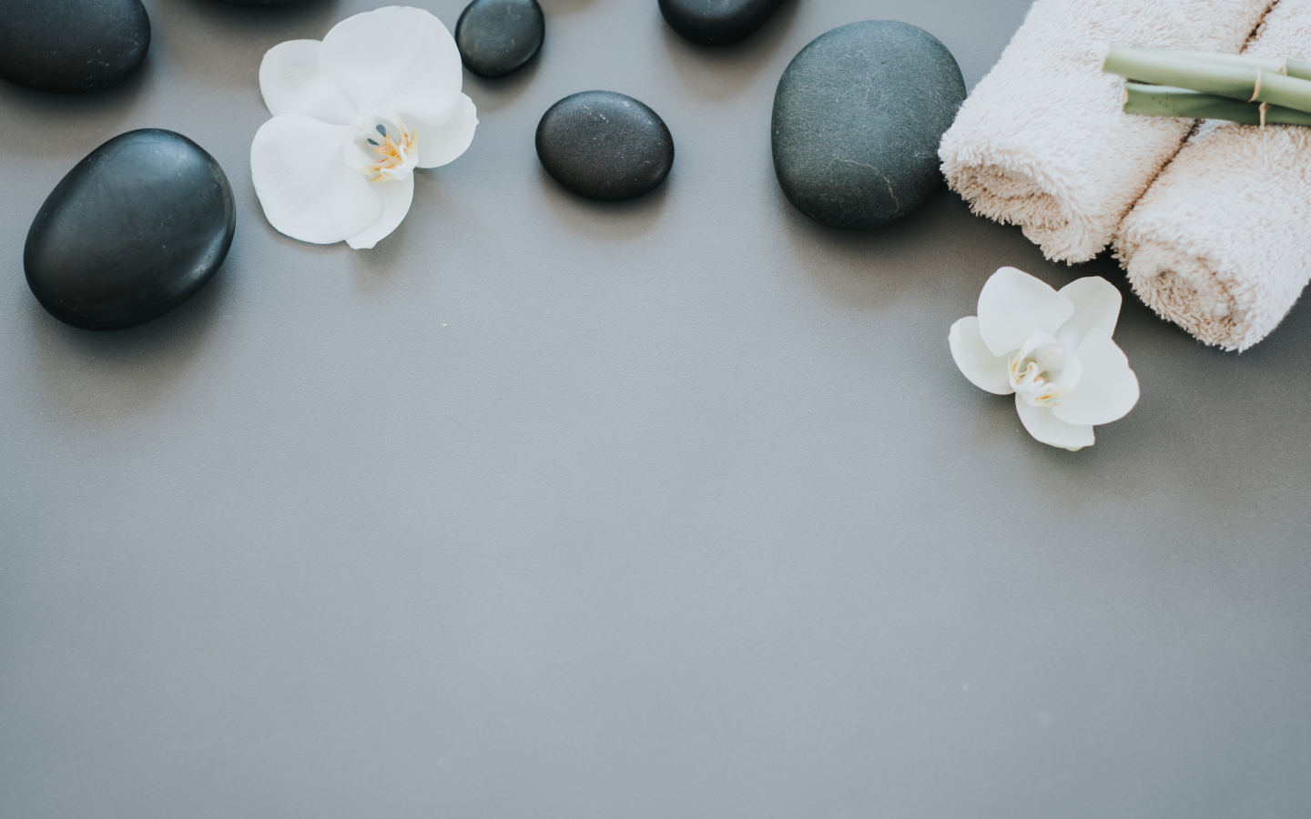 Черные камни с цветами орхидеи и полотенцем на сером фоне