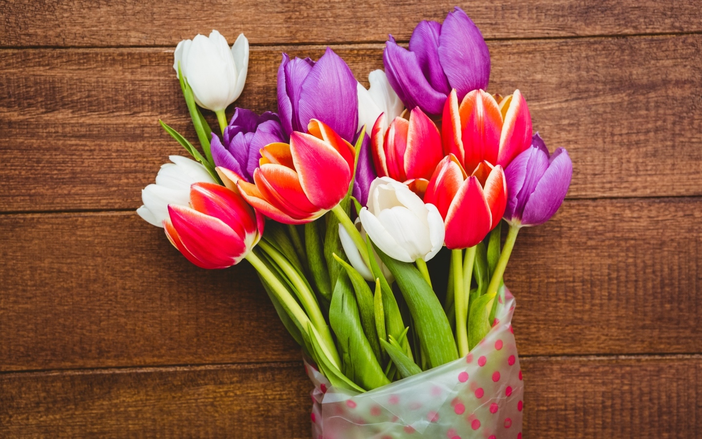 Букет разноцветных тюльпанов в пакете на деревянном фоне