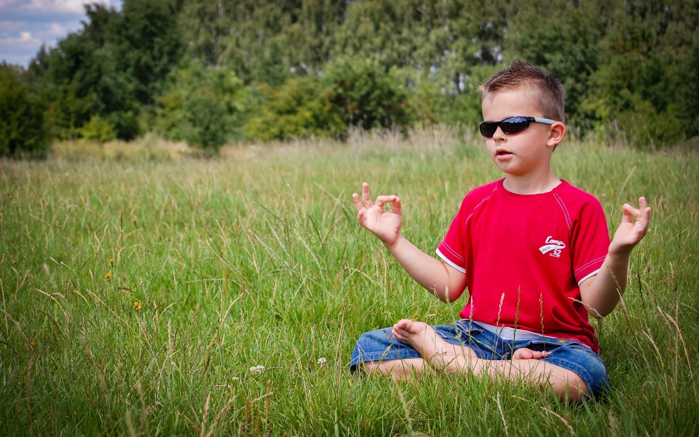 Маленький мальчик в очках медитирует на зеленой траве