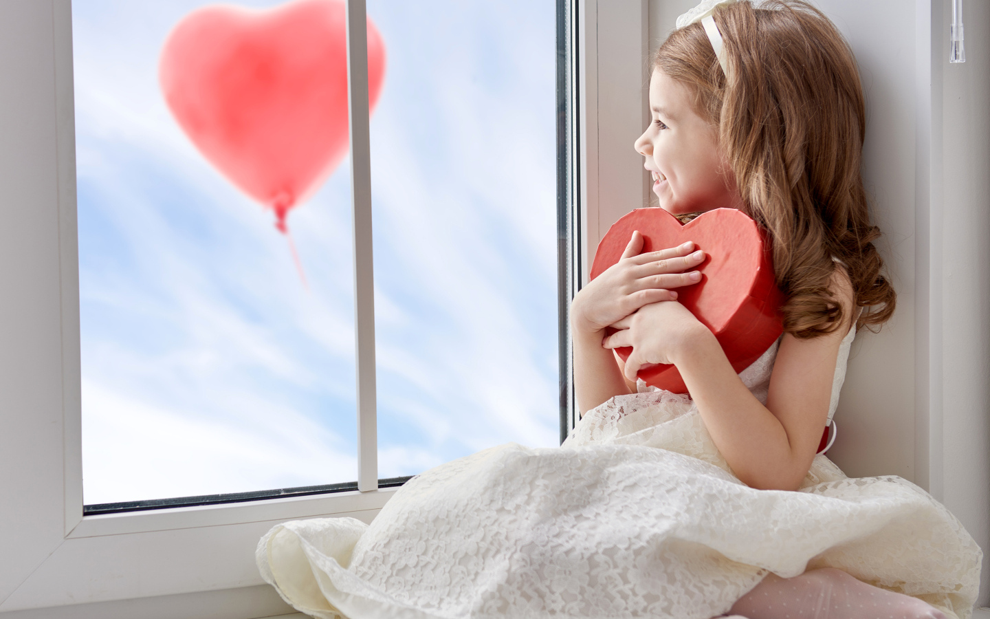 Маленькая девочка с коробкой в форме сердца сидит у окна