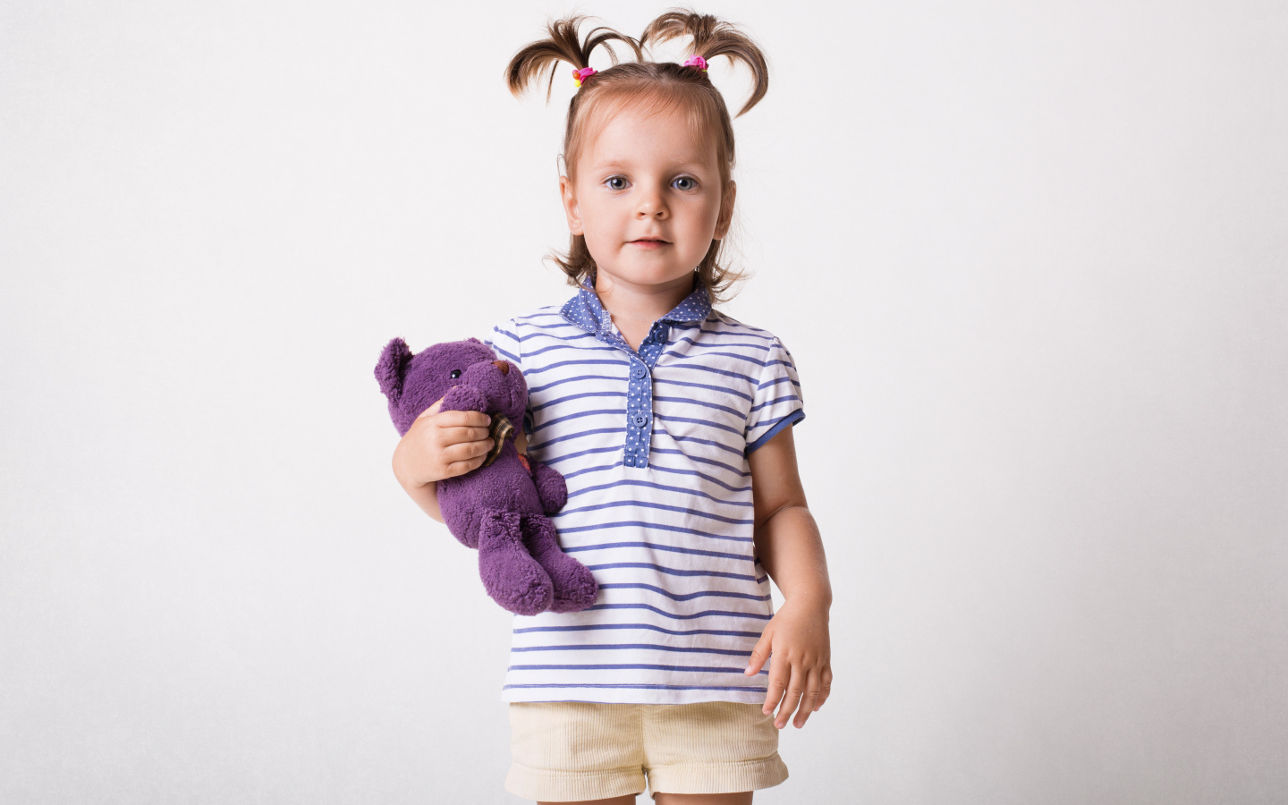 Маленькая девочка с игрушечным медведем на сером фоне