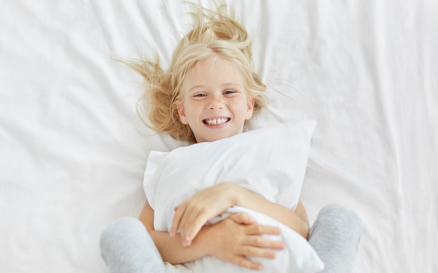Улыбающаяся маленькая девочка с подушкой на кровати
